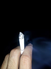 Close-up of hand holding cigarette over black background