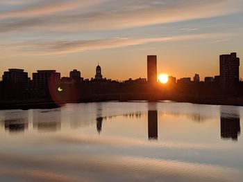 Scenic view of river by buildings against sky during sunset