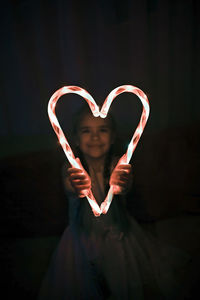 Midsection of woman holding heart shape against black background