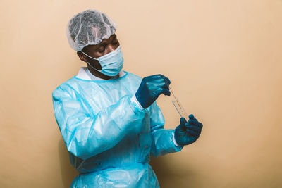 Doctor wearing protective suit and mask standing against yellow background