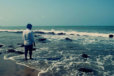 Rear view of man standing on beach against clear sky