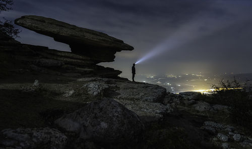 Silhouette man standing on rock against sky