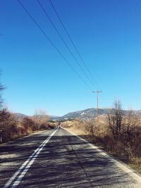 Road amidst trees against clear blue sky