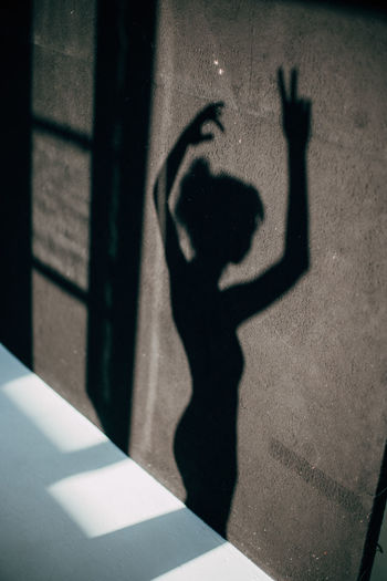 Shadow of woman with arms raised falling on wall