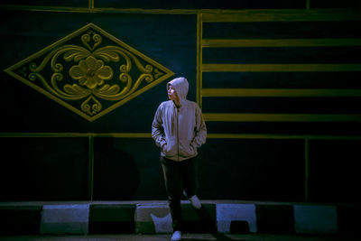 Full length of young woman standing against wall at night