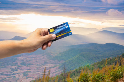 Midsection of person holding mobile phone against mountains