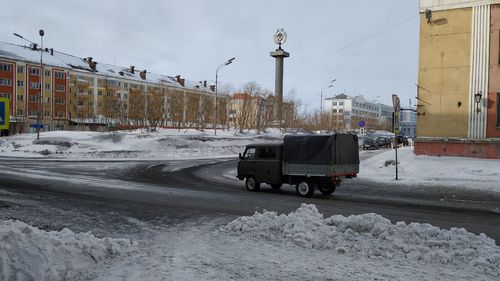 Cars on road by snow covered buildings against sky