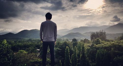 Rear view of man standing on mountain against sky