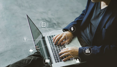 Digital composite image of businessman working on laptop with various symbols