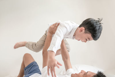 Father carrying son while lying on bed by wall at home