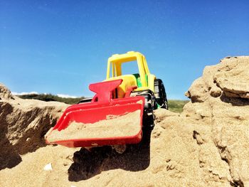 Close-up of toy bulldozer on sand against blue sky