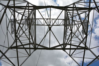 Directly below shot of electricity pylon against cloudy sky on sunny day