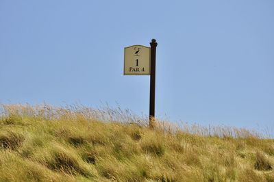 Low angle view of road sign on field against clear sky