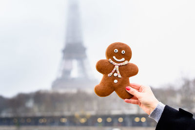 Cropped hand of woman holding gingerbread cookie against building