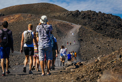 Rear view of people walking on dirt road during sunny day