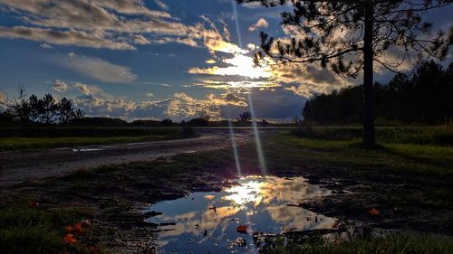 Puddle on field against sky at sunset