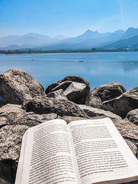 Open book on rock by sea against sky