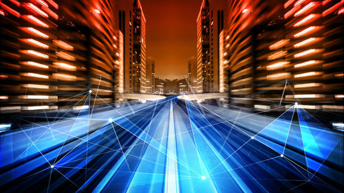 Digital composite image of illuminated light trails on building in city