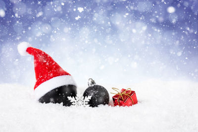 Close-up of christmas ornaments and santa hat on snow during winter