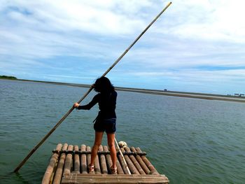 Rear view of woman rafting on sea against sky