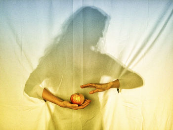 Woman with hands coming out and holding apple while standing against curtain