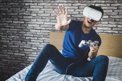 Cheerful man wearing virtual reality while sitting on bed at home