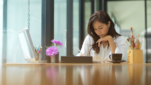 Young woman using phone while sitting on table