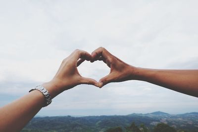 Cropped image of couple forming heart shape from hands against sky