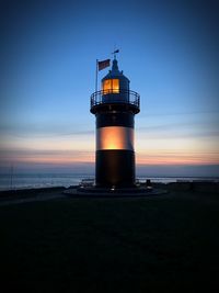 Lighthouse by sea against sky during sunset