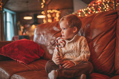 Portrait candid happy kid in knit beige sweater hold xmas mug with marshmallows and candy cane