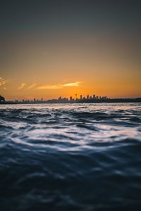 Scenic view of sea and urban skyline against sky during sunset