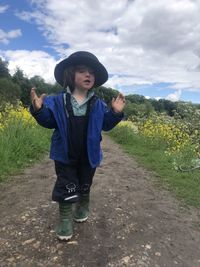 Boy with hat standing on path against sky