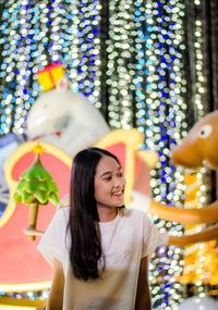 Smiling young woman against illuminated christmas decorations at night