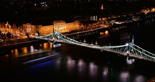 Illuminated bridge over river in city at night