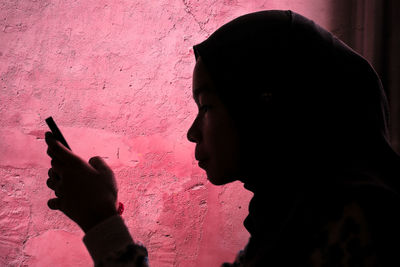 Side view of teenage girl using mobile phone against wall