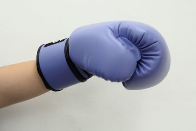 Cropped hand wearing purple boxing glove against white wall