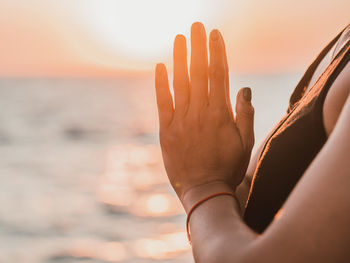 Close-up of hand by sea against sky during sunset