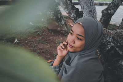 High angle view of thoughtful young woman wearing hijab sitting outdoors