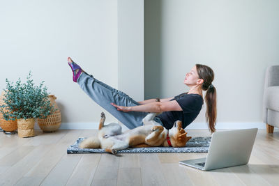 Doga concept.young woman in yoga position balancing with her dog. home online training with a pet