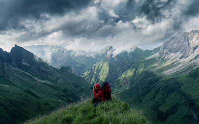 Woman sitting on mountain against cloudy sky