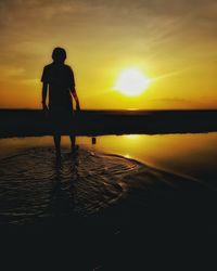 Silhouette man standing on beach against sky during sunset