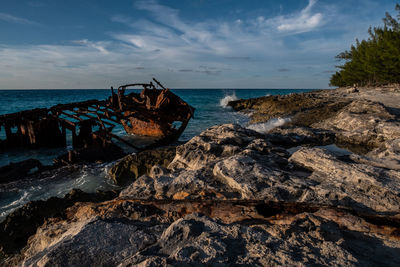 View of shipwreck and rocks on a beach against sky