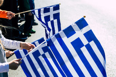 Midsection of woman holding greek flags while standing on road