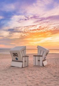 Hooded beach chair on shore against sunset sky