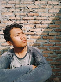 Young man with eyes closed sitting against brick wall