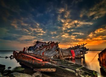 Abandoned boat moored at beach against sky during sunset