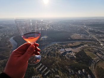 Man holding glass of cityscape against sky