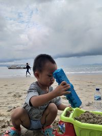 Boy holding toy on beach against sky