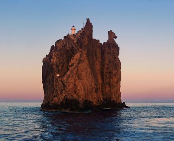 Rock formation in sea against clear sky