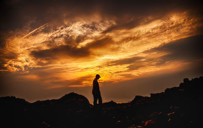 Silhouette man standing on rock against sky during sunset